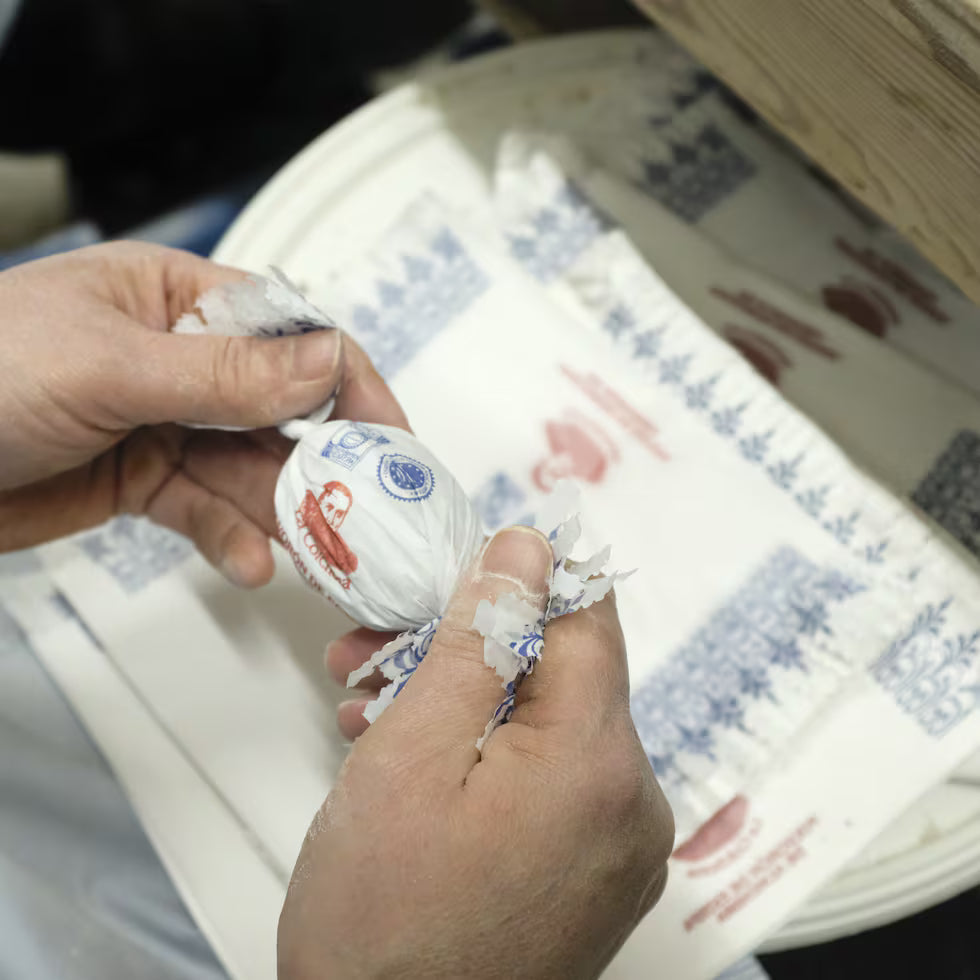 Hands wrapping a polvorón in printed paper at the La Colchona bakery in Estepa